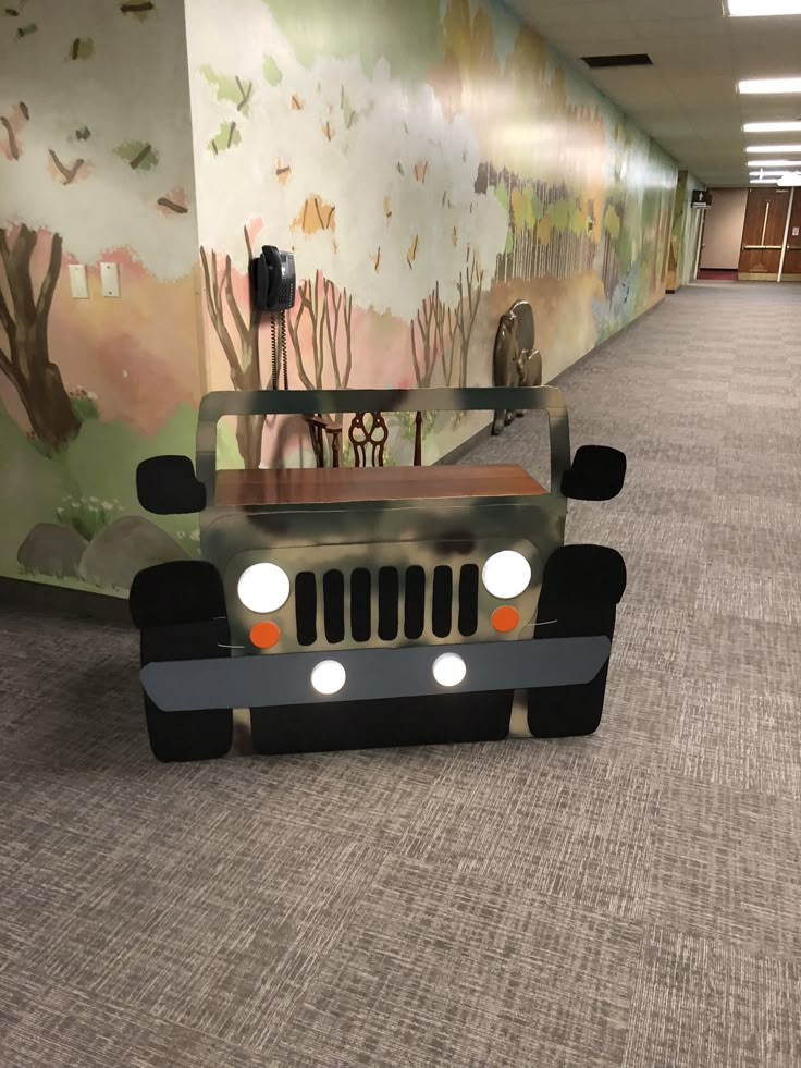 a car made out of cardboard sitting in the middle of a hallway with murals on the walls