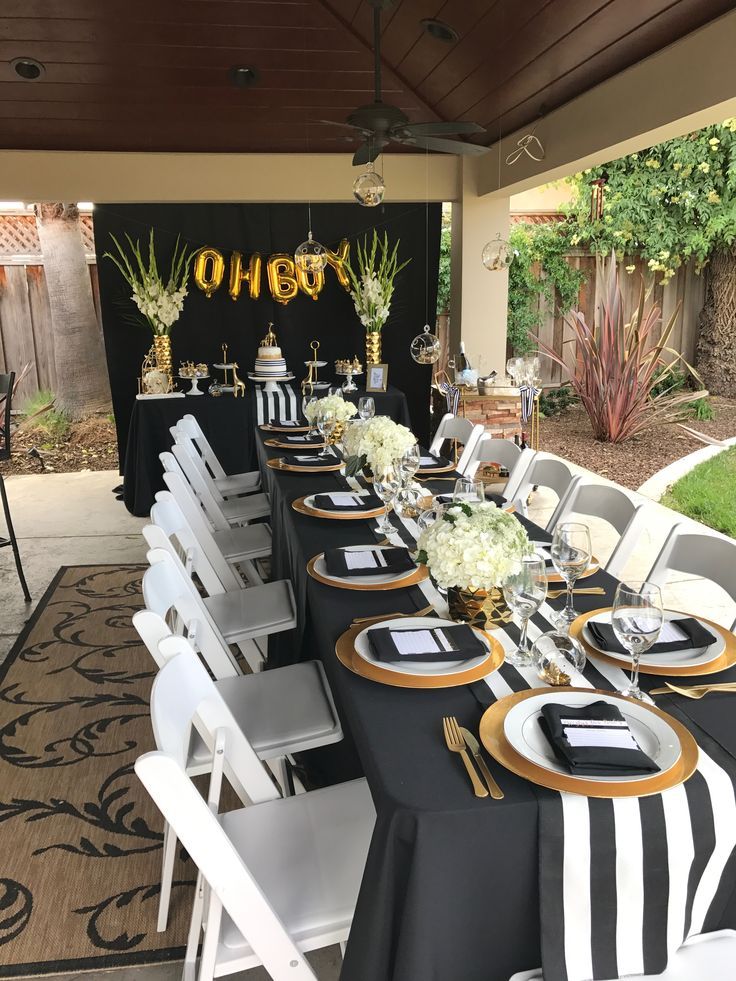 a long table set up with black and white tables cloths, gold plates and silverware