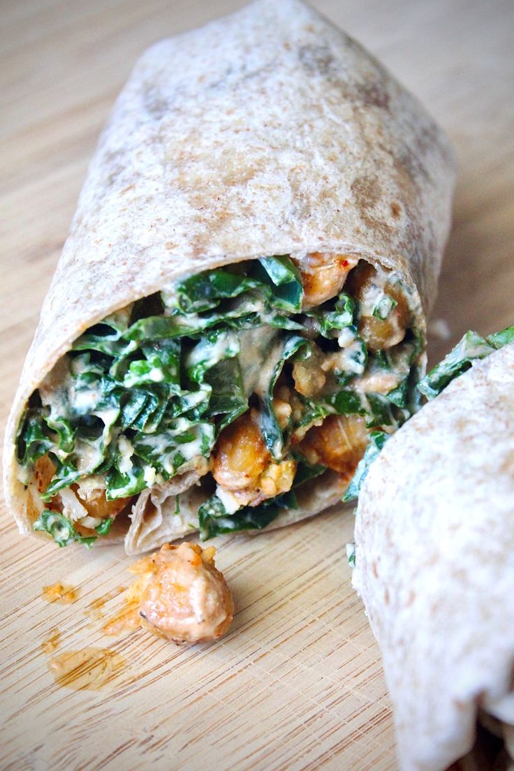 a wrap filled with spinach and chicken on top of a wooden table