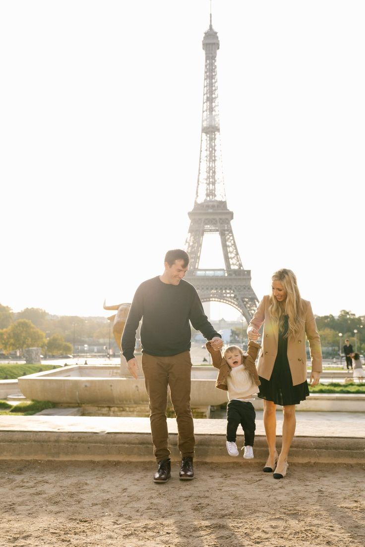 a man, woman and child are standing in front of the eiffel tower