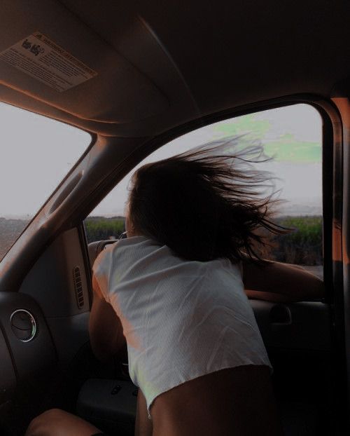 a woman sitting in the driver's seat of a car with her hair blowing in the wind