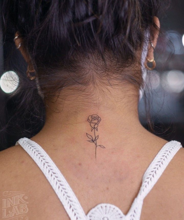 a woman's back neck with a small rose tattoo on the left side of her neck