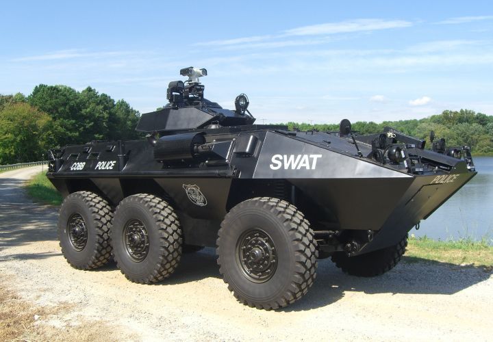 an armored swat vehicle parked on the side of a road next to a body of water