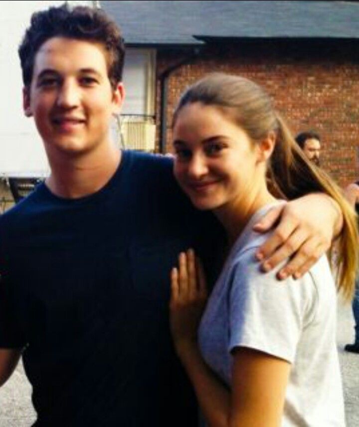 a man and woman standing next to each other in front of a building with people