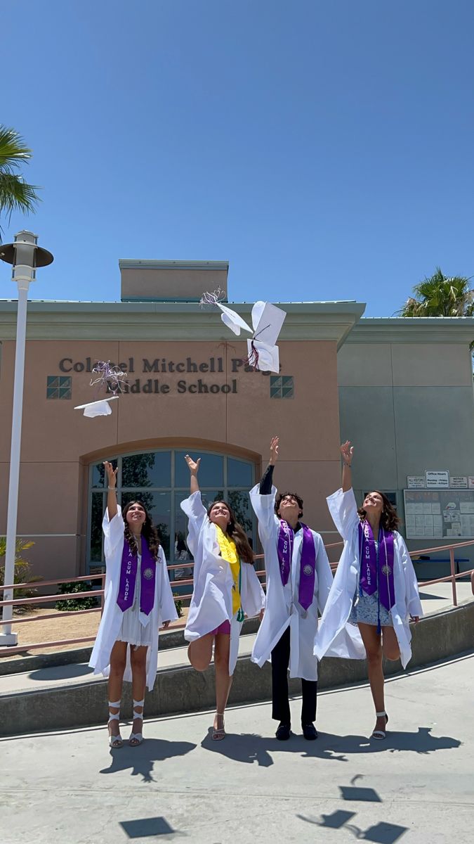 four girls in graduation gowns are posing for the camera outside of a school building