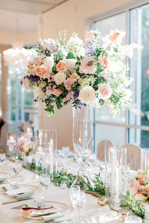 an elegant table setting with flowers in a tall glass vase on the centerpieces