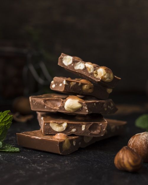 chocolate bars stacked on top of each other with nuts and mint leaves around them next to a glass of water