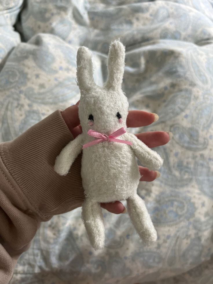 a hand holding a small white stuffed animal with a pink ribbon around it's neck