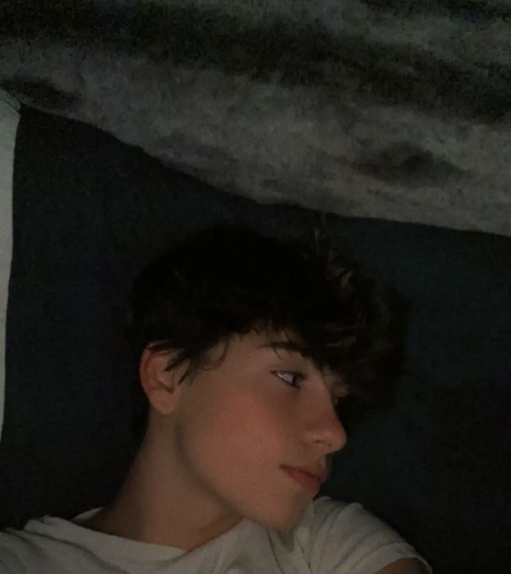 a young boy laying in bed with his eyes closed and looking at something on the ground