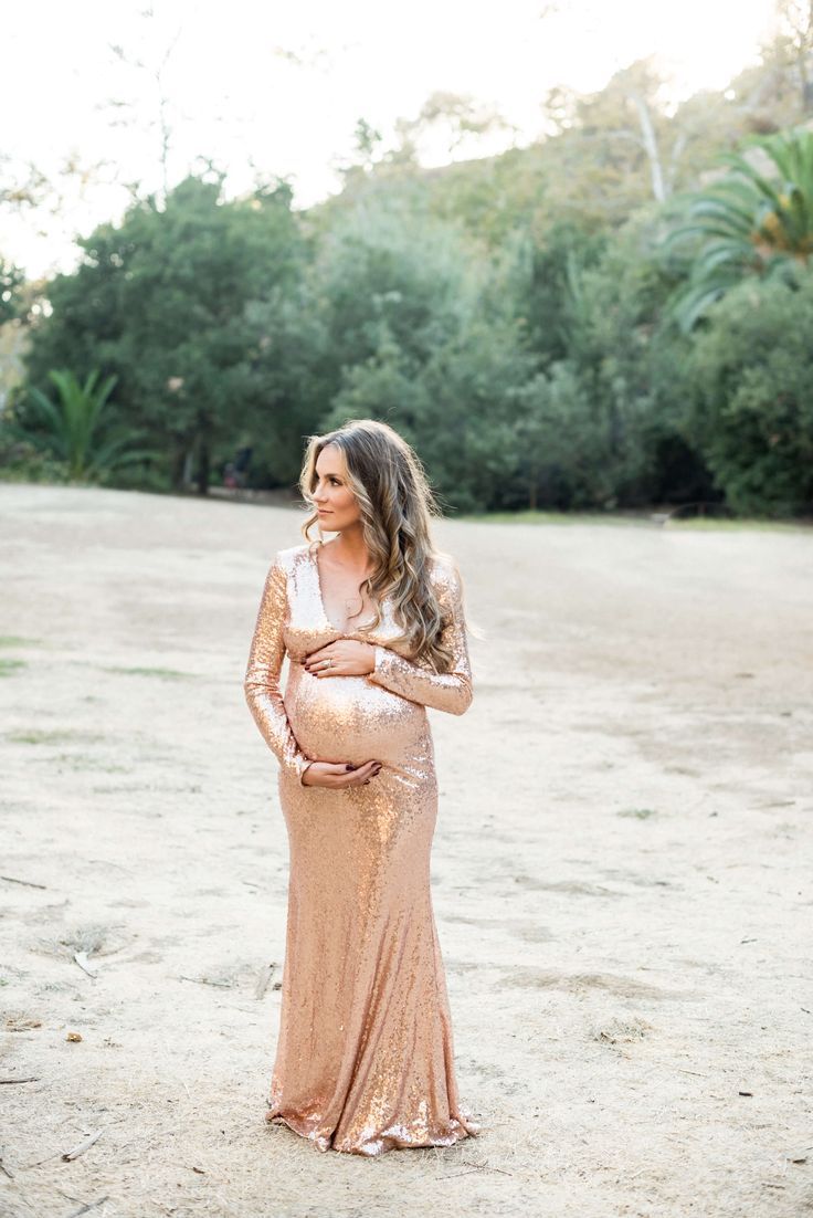 a pregnant woman standing in the sand with her hands on her stomach and wearing a gold dress