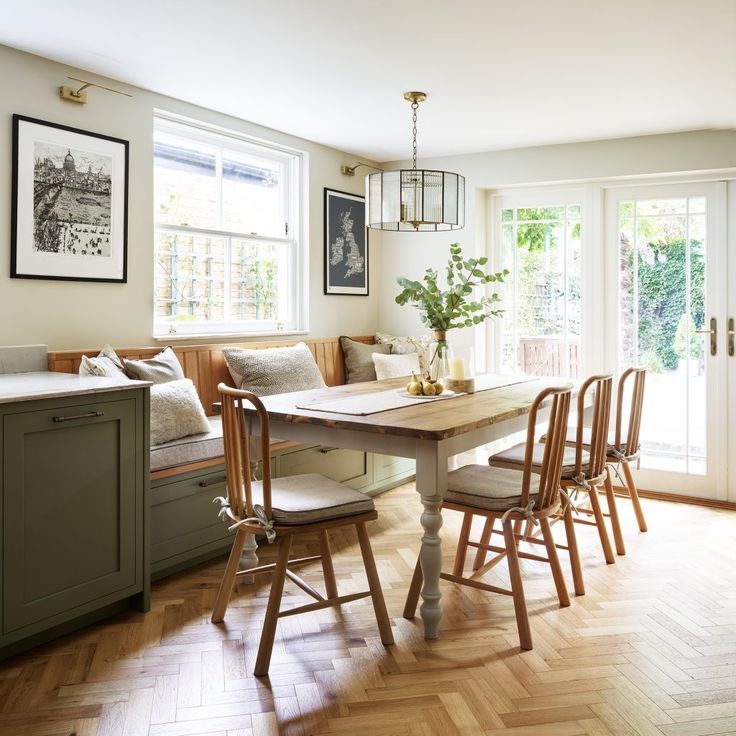 a dining room table with four chairs and a bench in front of two windows that look out onto the backyard