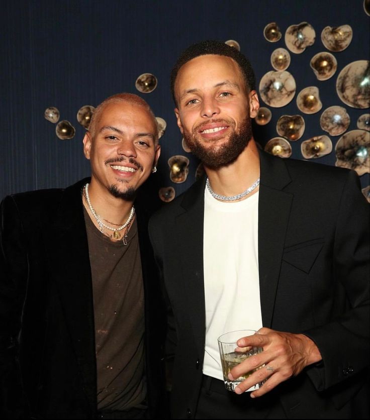 two men standing next to each other holding drinks in front of a disco ball wall