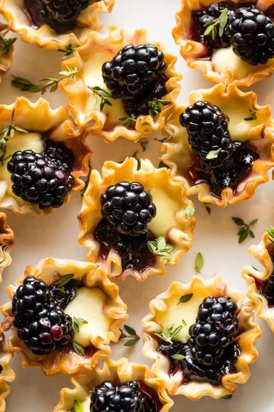 blackberries and cream pies are arranged on a white platter with fresh herbs