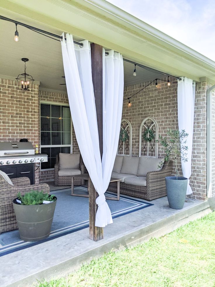 an outdoor living area with patio furniture and white drapes on the side of the house