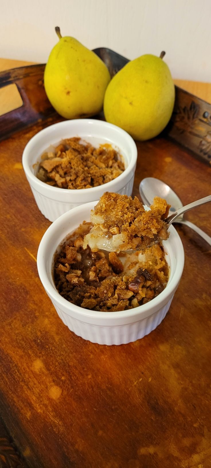 two bowls filled with granola on top of a wooden table next to pears