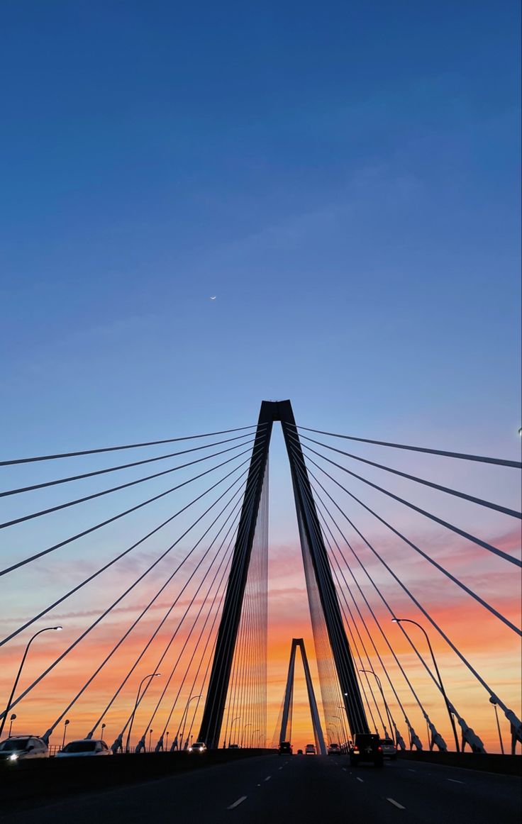 the sun is setting behind a tall bridge