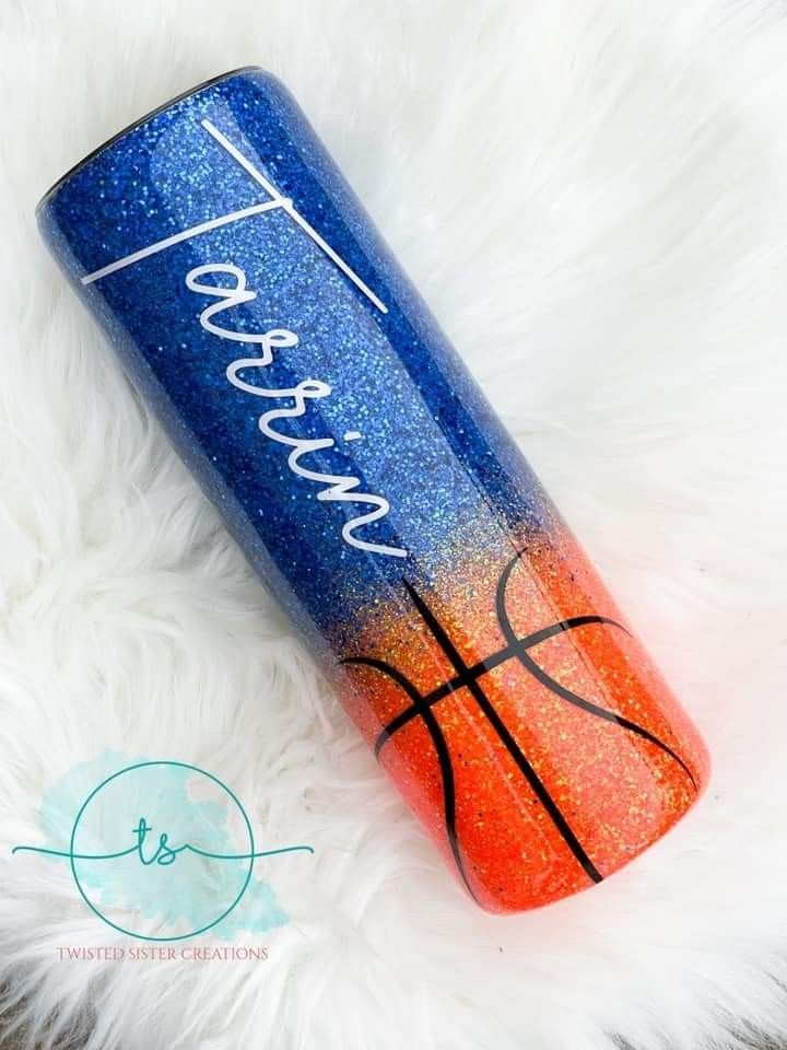 a blue and orange glitter tumbler with a basketball on it sitting next to a white fur rug