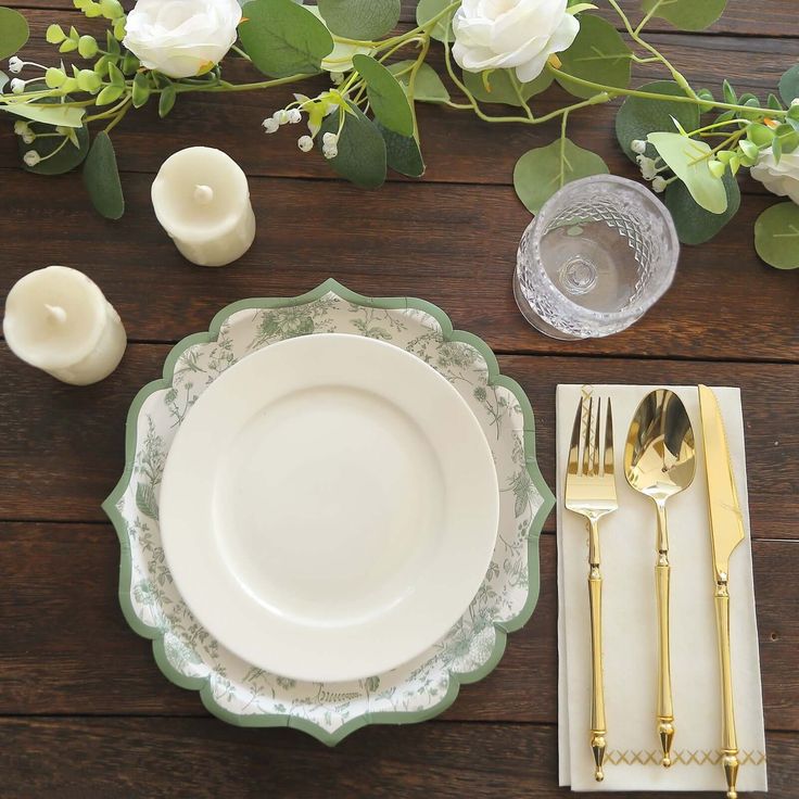 a place setting with flowers and candles on a wooden table top, next to silverware