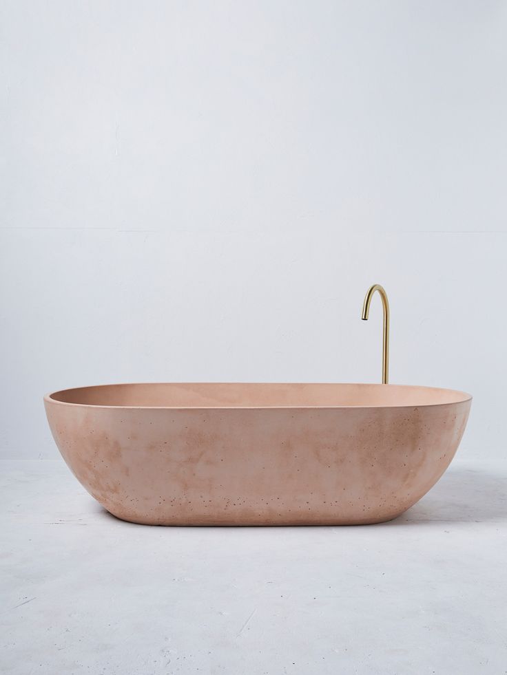 an oval bathtub with a gold faucet sits on a white surface, in front of a plain wall