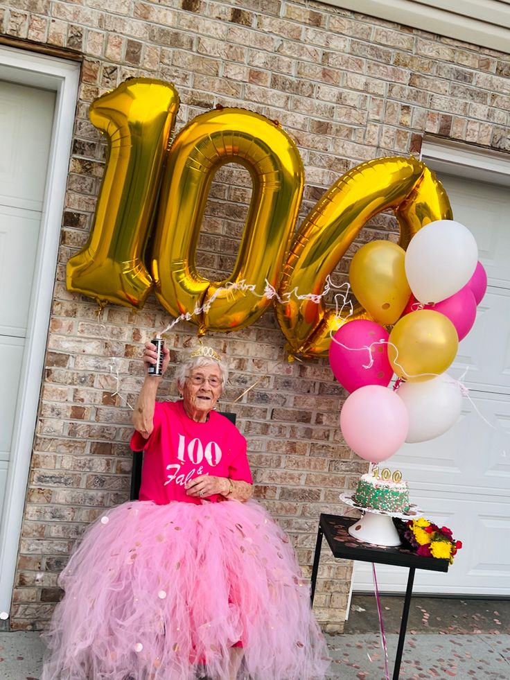 a woman sitting on a chair in front of a brick wall with balloons and streamers