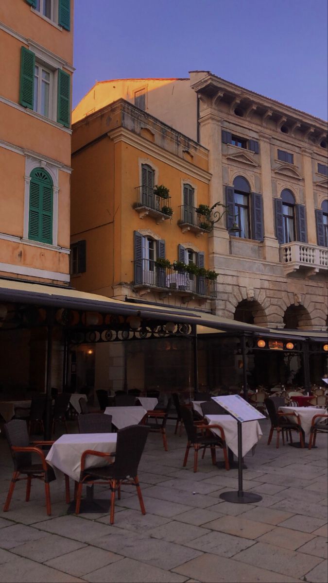 an outdoor dining area with tables, chairs and umbrellas on the sidewalk in front of buildings