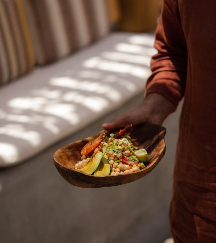 a person holding a wooden bowl filled with food on top of a table next to a couch