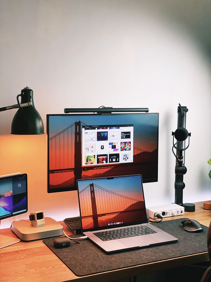 a desk with two laptops and a desktop computer on it, in front of a lamp