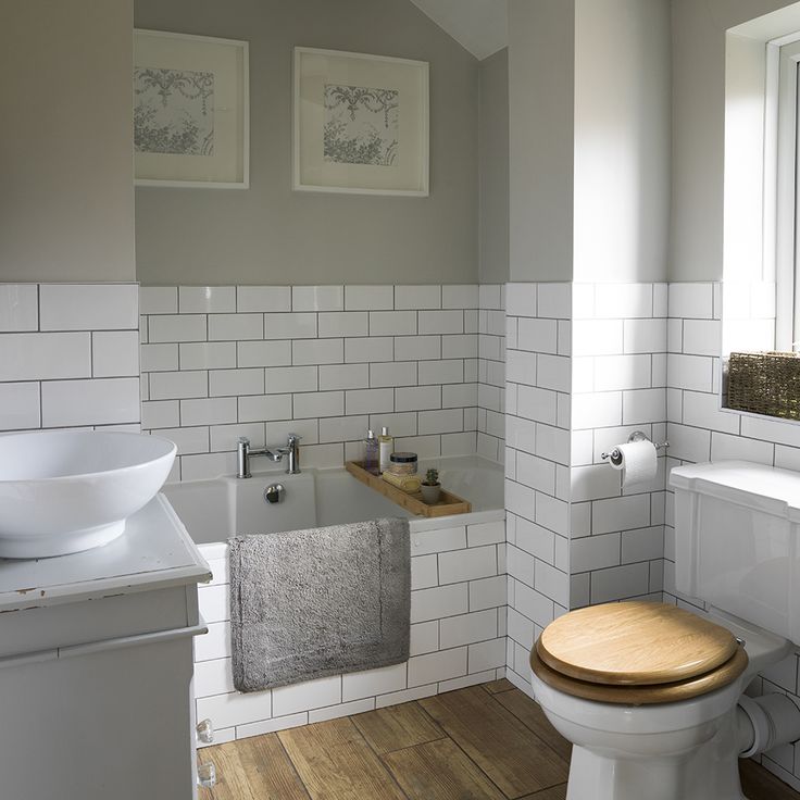 a bathroom with white tile walls and wood flooring