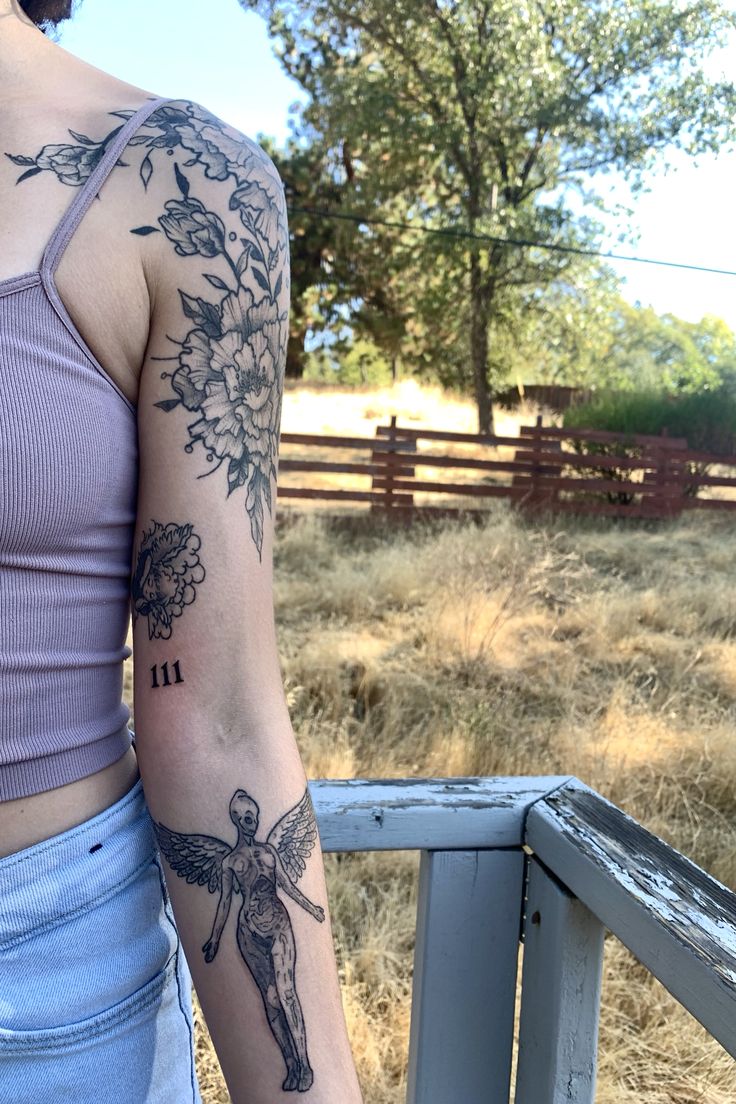 a woman with a tattoo on her arm standing next to a wooden fence and looking off into the distance