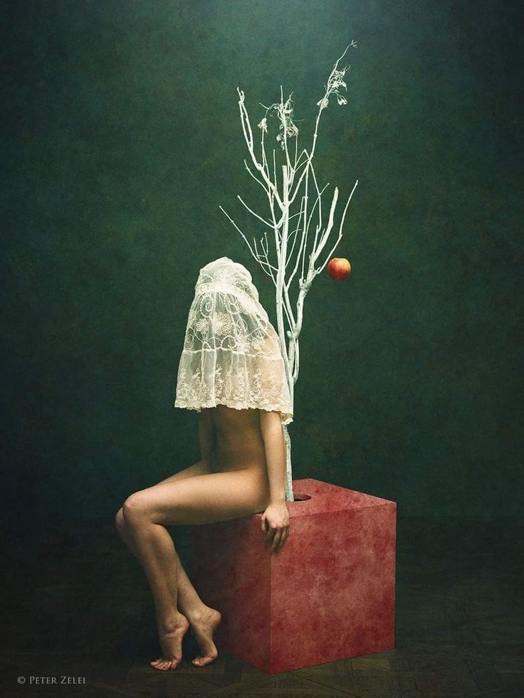 a woman sitting on top of a red box next to a tree