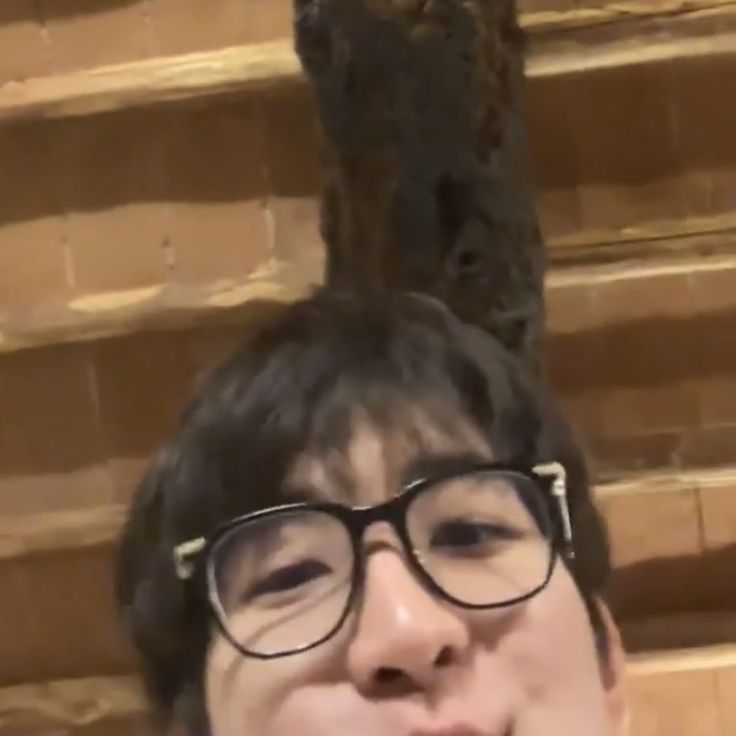 a man with glasses making a funny face in front of a wooden wall and tree trunk