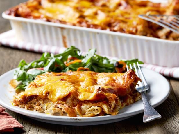 a white plate topped with lasagna next to a green salad and a fork