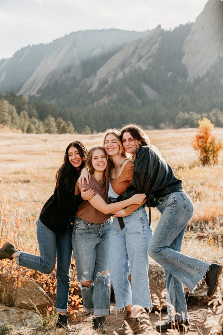 three girls hugging each other in the middle of a field with mountains in the background