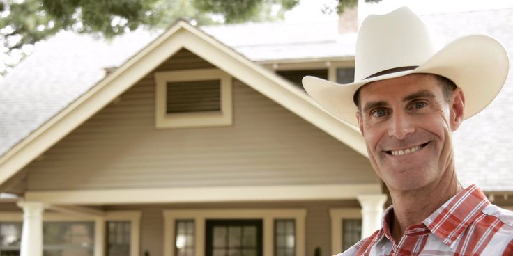 a man wearing a cowboy hat standing in front of a house with a red and white checkered shirt