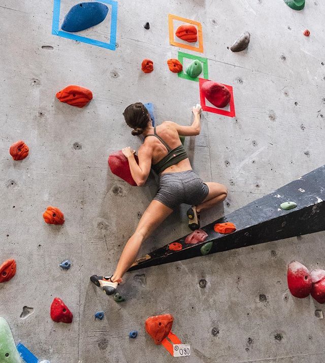 a woman climbing up the side of an indoor climbing wall with colorful rocks on it