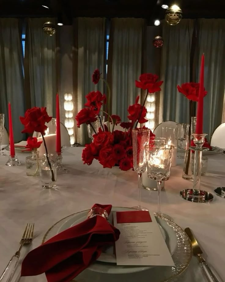 the table is set with silverware and red flowers in vases, candles and napkins