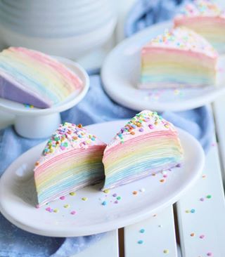 two slices of rainbow cake on plates with sprinkles