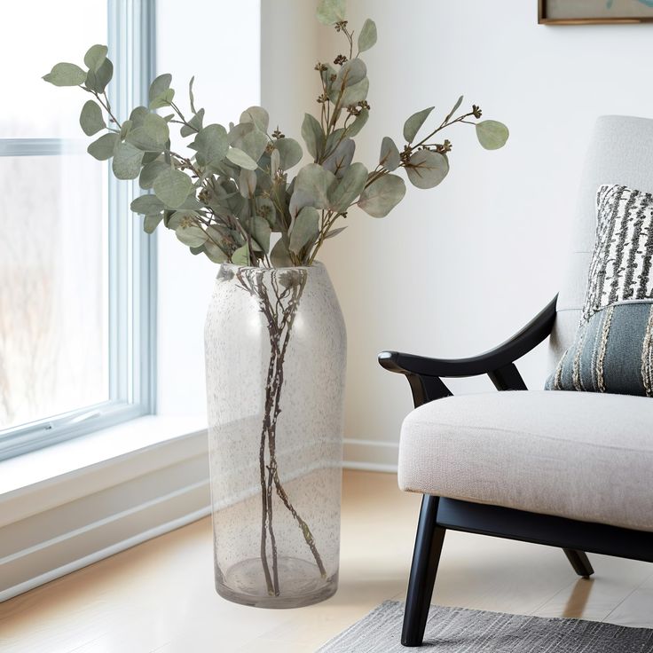 there is a vase with flowers in it on the floor next to a chair and window