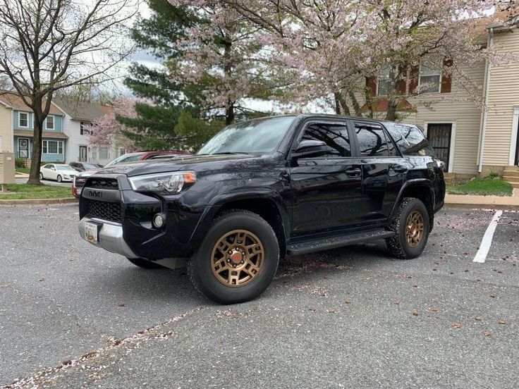 a black truck with gold rims parked in front of a house on a street