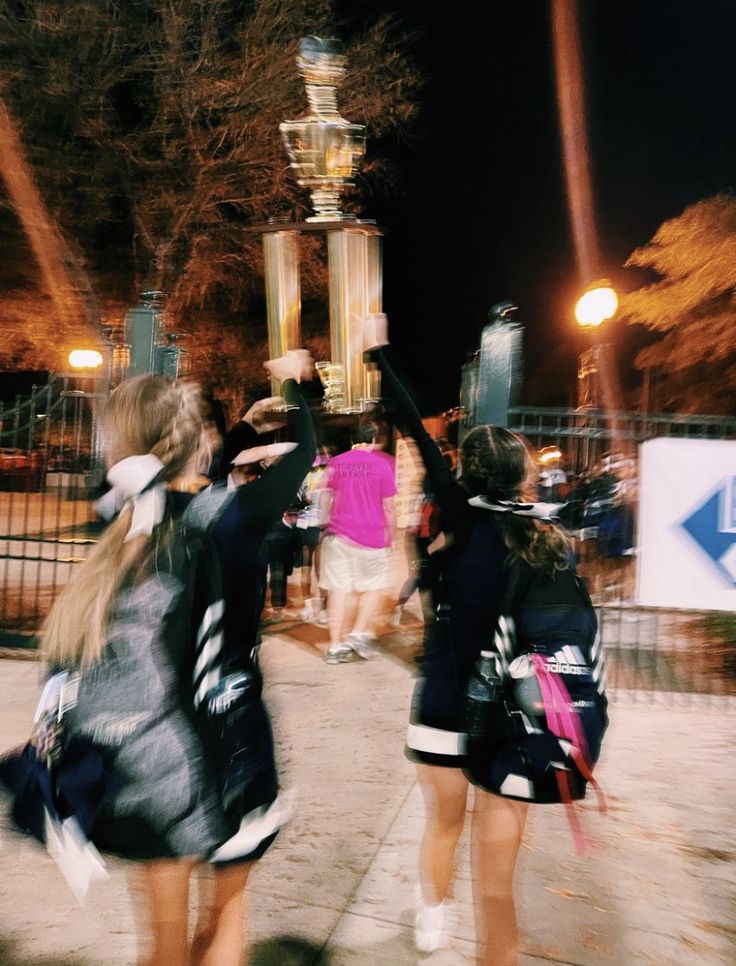 two girls are walking down the sidewalk with their arms in the air