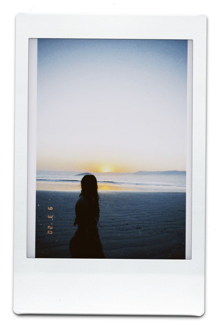 a polaroid photo of a person standing on the beach at sunset, with an ocean in the background