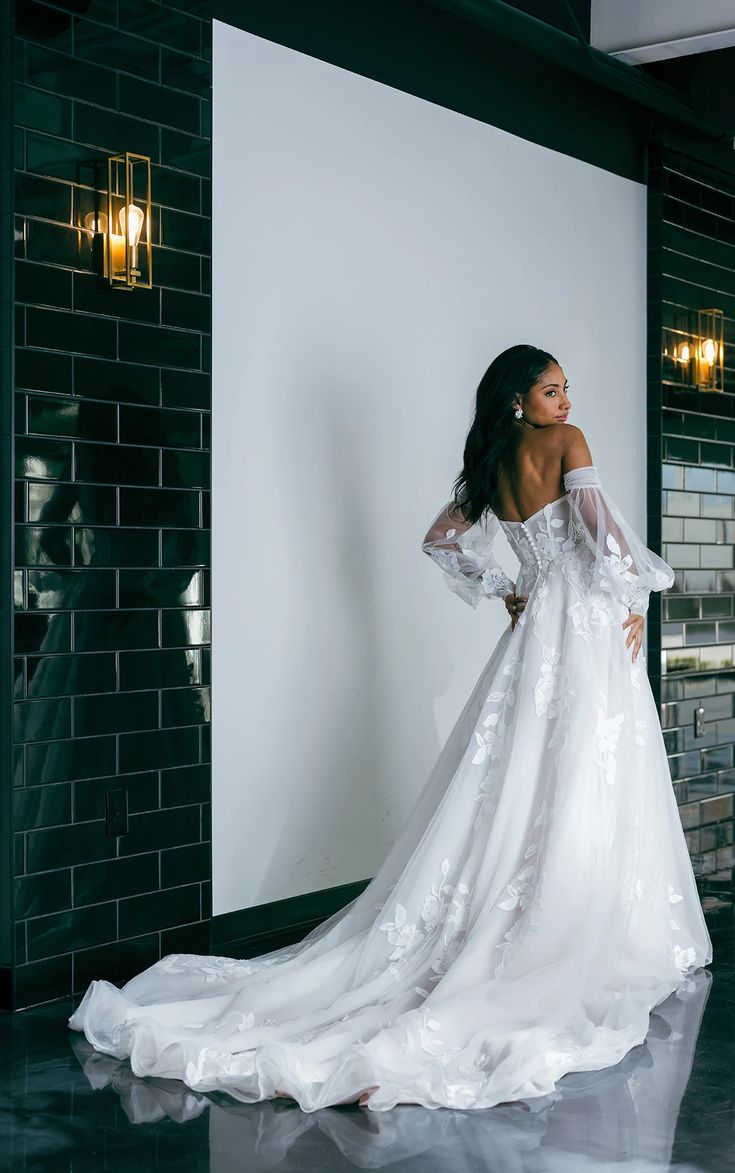 a woman in a white wedding dress is standing near a wall and looking off to the side