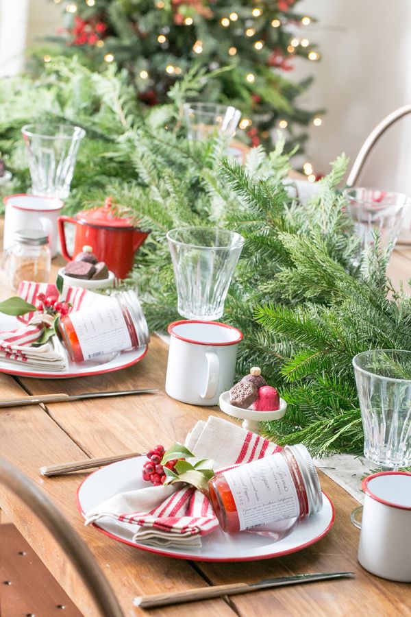 the table is set for christmas dinner with red and white plates, silverware, holly wreaths and candlesticks