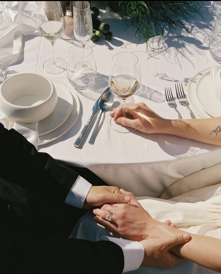 the bride and groom are holding hands at their wedding dinner table with white linens