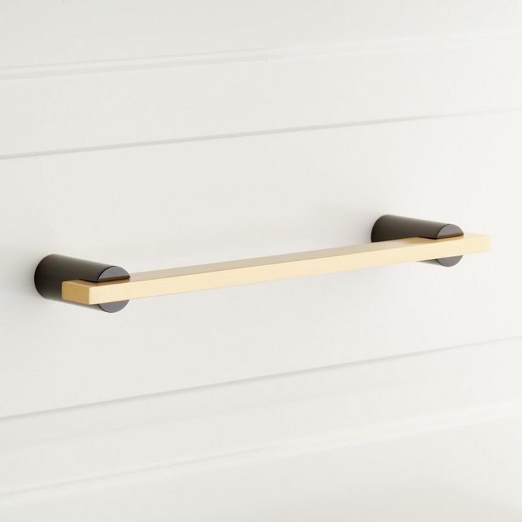 an image of a brass and black towel bar on a white painted wood paneled wall