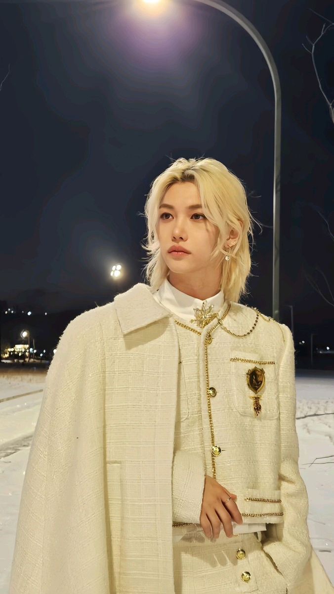 a woman with blonde hair wearing a white coat and standing in the snow at night