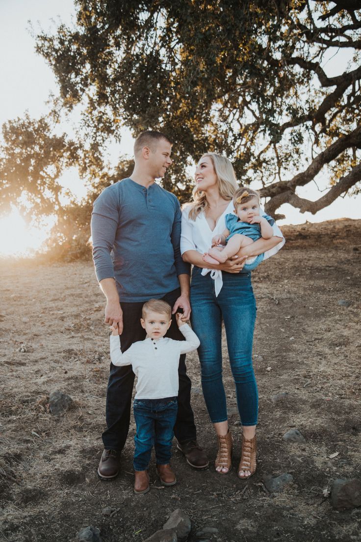 a family standing in front of a tree with the sun shining on them and holding their baby