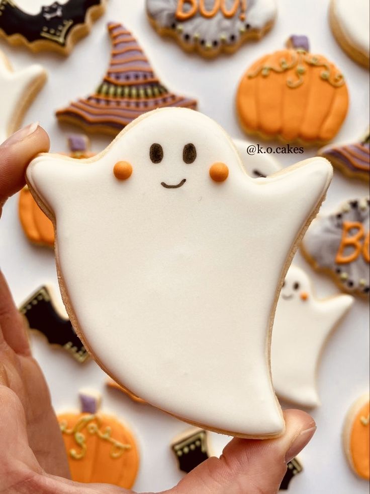 a hand holding a decorated halloween cookie in front of some cookies with ghost faces on them