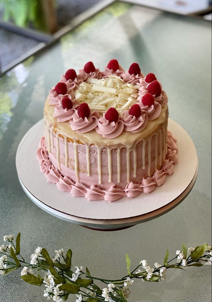 a cake sitting on top of a white plate covered in frosting and raspberries