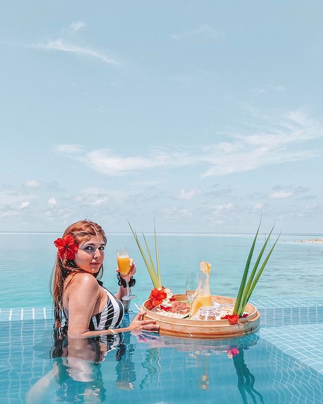 a woman sitting on the edge of a swimming pool holding a glass of orange juice